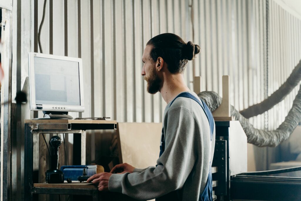 Logiciel location matériel : un utilisateur en bleu de travail consulte son poste informatique dans l'atelier
